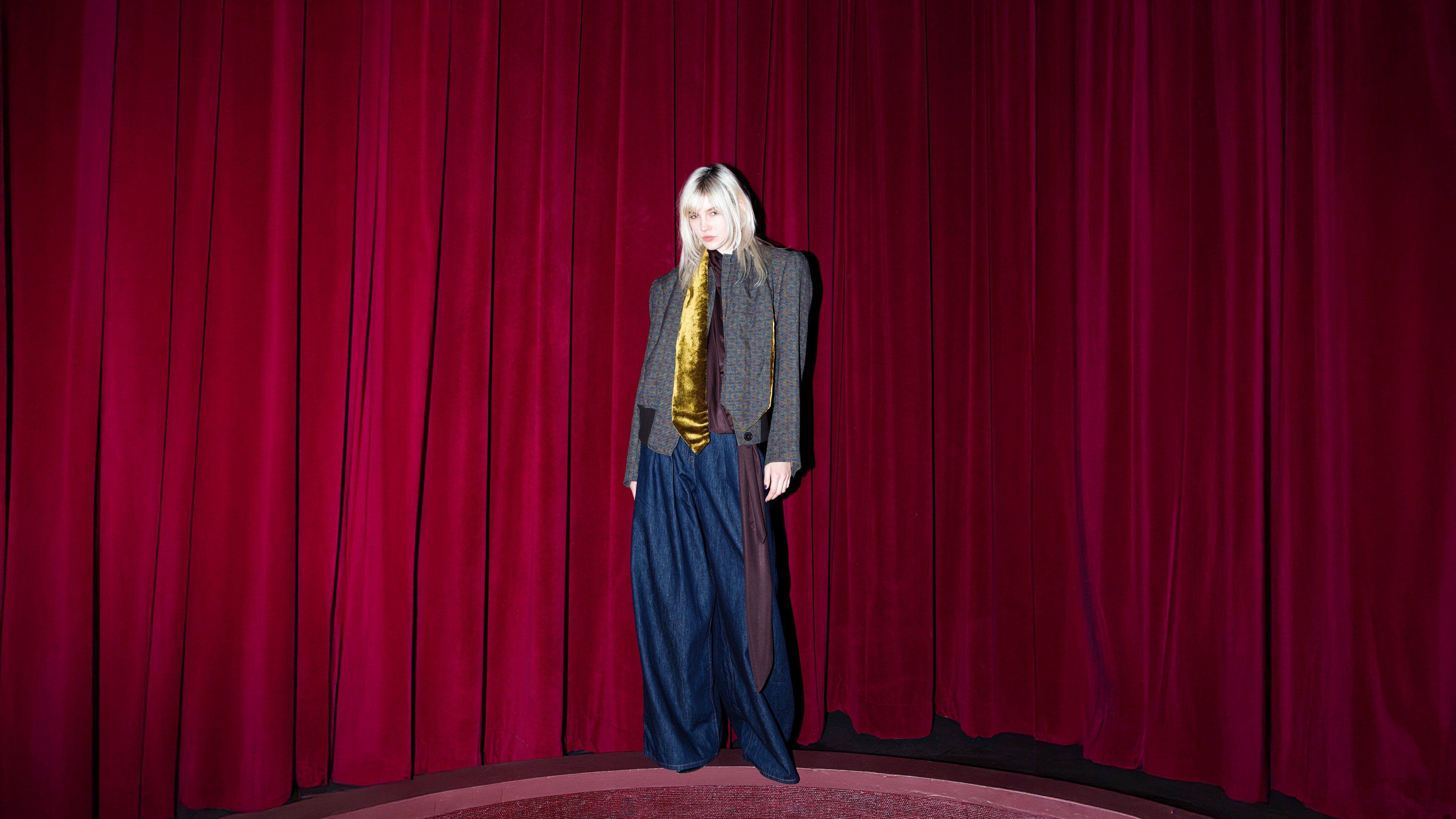 Dries Van Noten FW25 look on model posed against dramatic red theater curtains